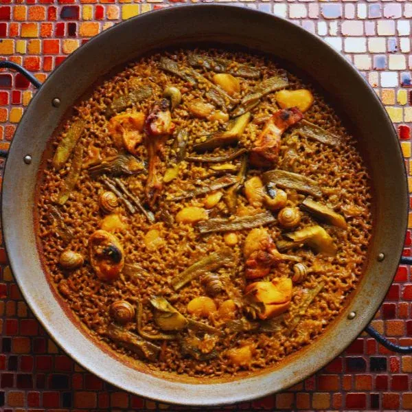 Paella valenciana dans sa poêle, sur un fond de mosaïque colorée